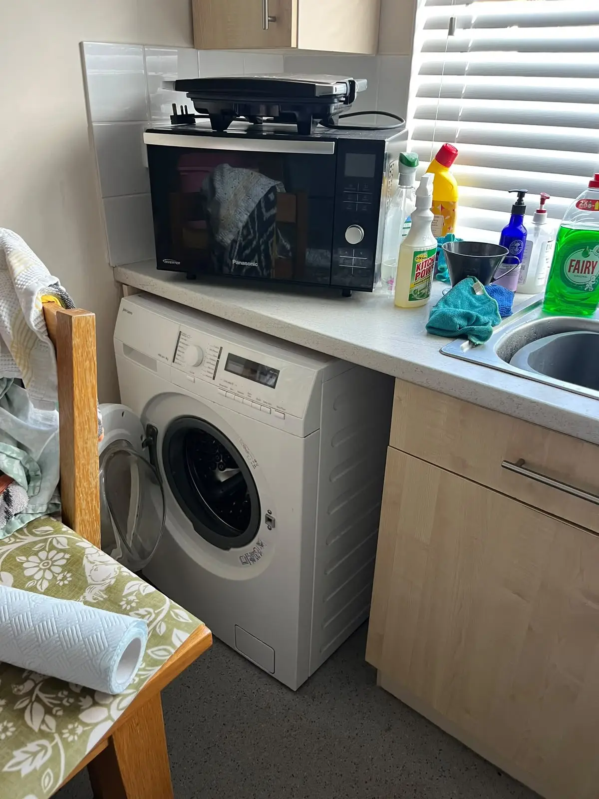 Kitchen before clearance — microwave, washing machine and cleaning products